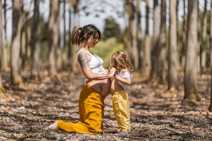 Pregnant mother and little daughter having fun in park