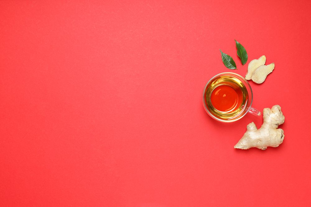 Cup of tea and ginger on red background, space for text