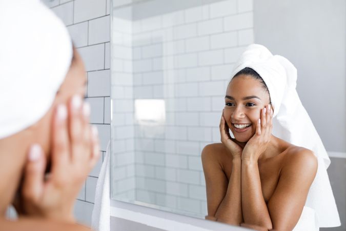 Radiant Black woman in towel touching her face in the mirror