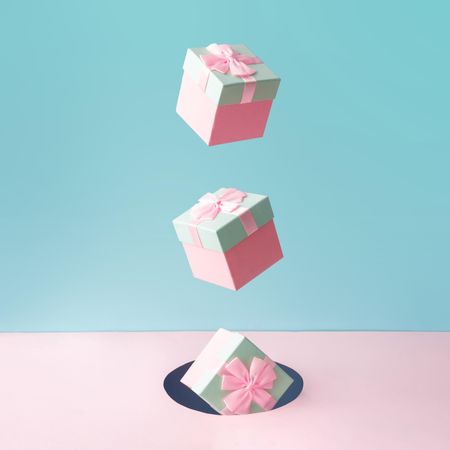 Pastel pink Christmas gift boxes on blue and pink backdrop falling into a hole