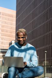 Stylish young Black man working remotely on laptop in city park