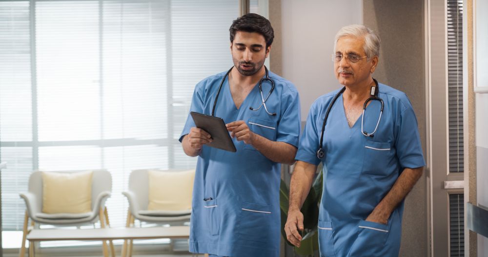Portrait of Indian Young and Male Doctor and Nurse Using a Digital Tablet and Talking in Hospital Corridor.
