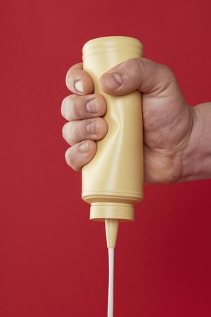 Squeezing a mayonnaise bottle isolated on a red background