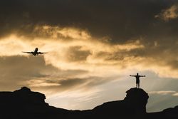 Human silhouette on hill delighting in view of aircraft in sky