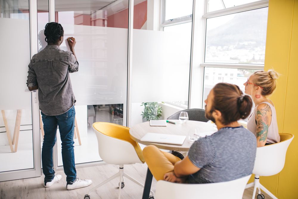 One man standing at a white board giving a presentation to his 2 colleagues