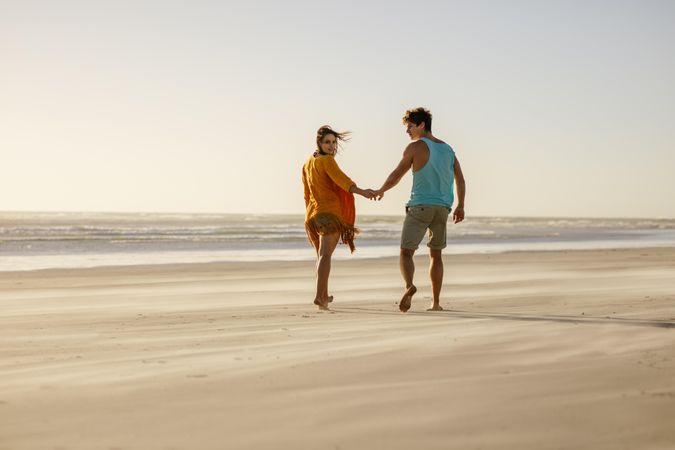 Rear view of happy couple walking on beach bare feet