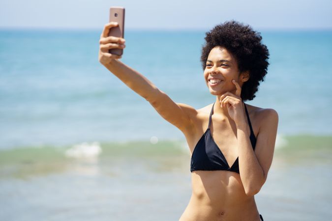 Happy woman in bikini taking selfie on phone on coast