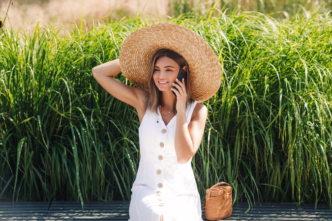 Woman sitting in front of long grass looking away while on cell phone