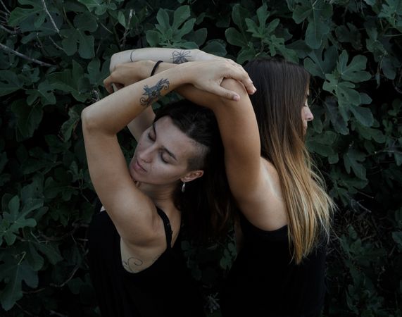 Young women posing near green bush