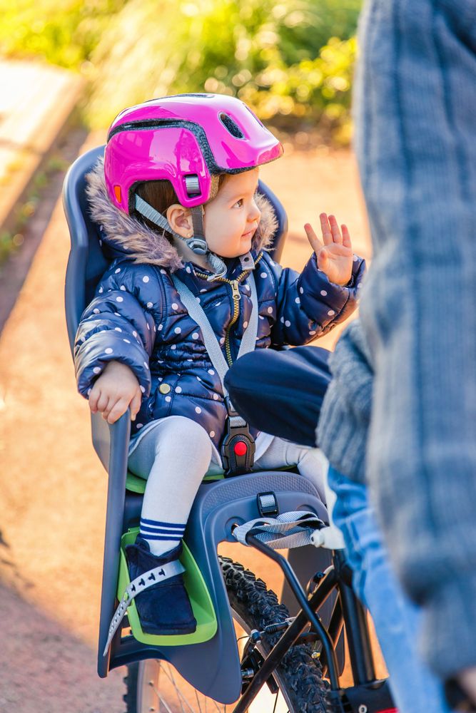 Portrait of little girl with pink helmet on waving in bike seat in back of ride