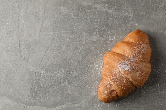 Croissant with powdered sugar on grey background, top view, copy space