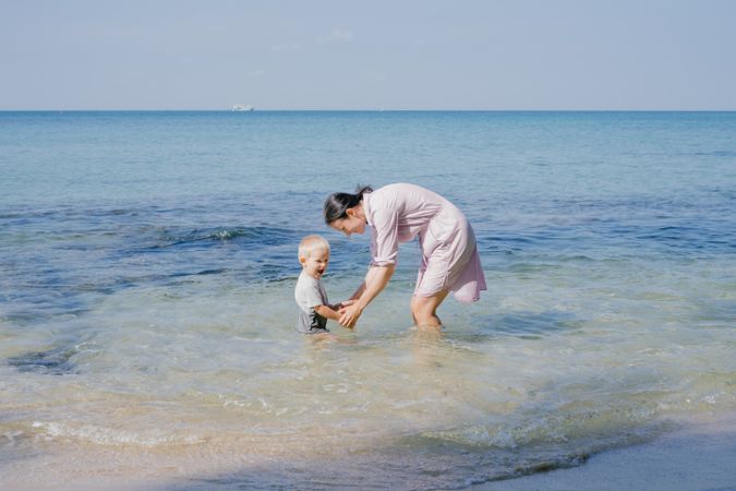 Woman and small kid having fun with water while relaxing on seacoast at resort