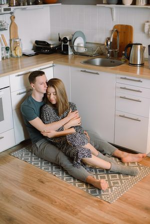 Man and woman hugging and sitting on mat on kitchen floor