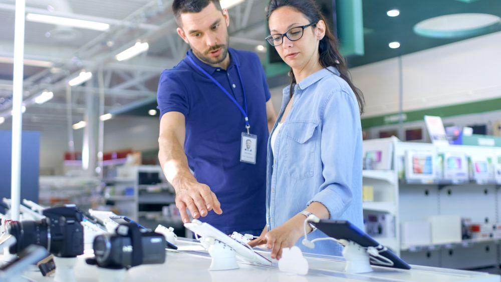 In the Electronics Store Consultant Gives Professional Advice to a Young Woman, She Considers Buying New Tablet Computer and Needs Expert Opinion.