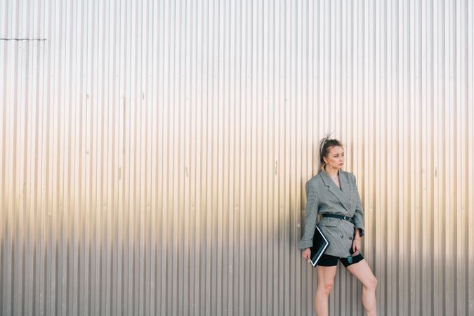 Woman with tablet in stylish suit standing nearby wall holding sunglasses