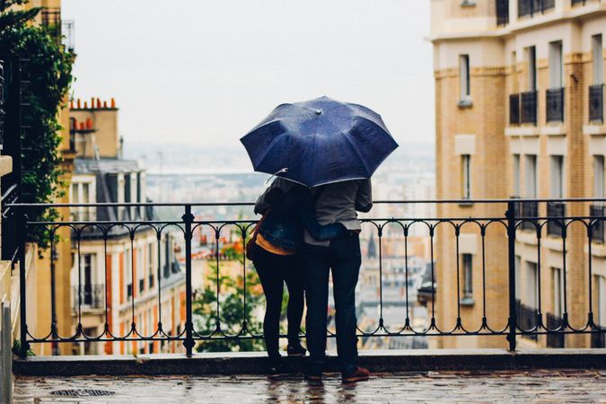 Backside of man and woman standing under umbrella while raining