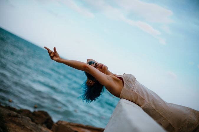 Gracious woman in sundress lying on back on parapet and reaching out for ocean