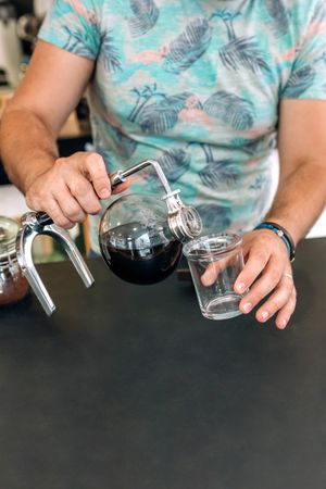 Unrecognizable barista pouring specialty coffee from Japanese siphon coffee maker into a glass