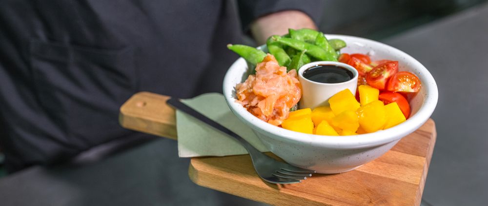 Close up of unrecognizable chef showing freshly colorful poke bowl with salmon on restaurant kitchen