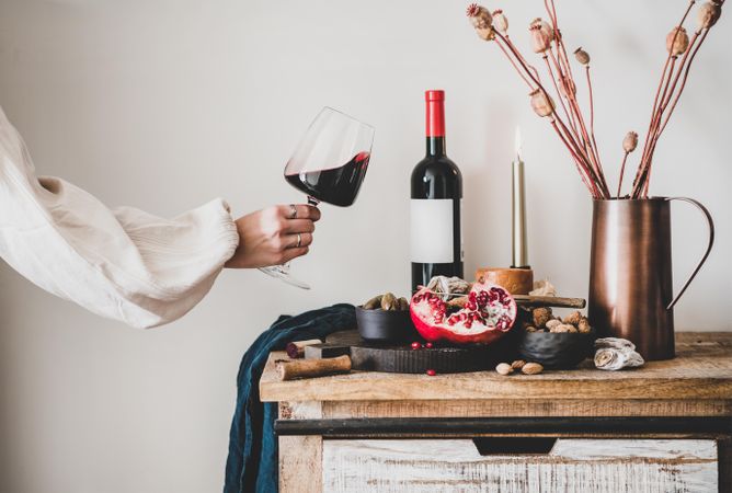 Rustic setting of women swirling wine, with cheese, long candles, pomegranate, and dried poppies