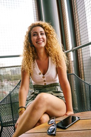 Smiling woman sitting in designed metal chair with sunglasses in hand