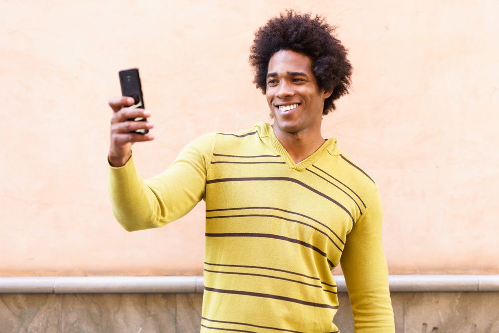 Man taking picture with his phone against peach wall