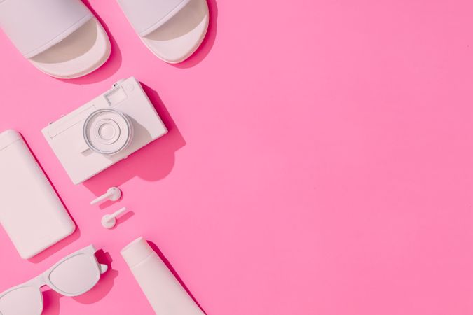 Summer objects of sunglasses, camera, smart phone and sunscreen, EarPods on pink background