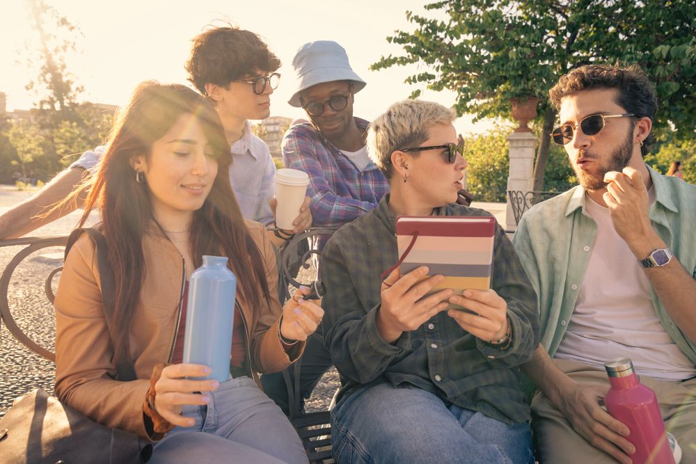 Diverse group of students collaborating with a laptop outdoors on a park bench.