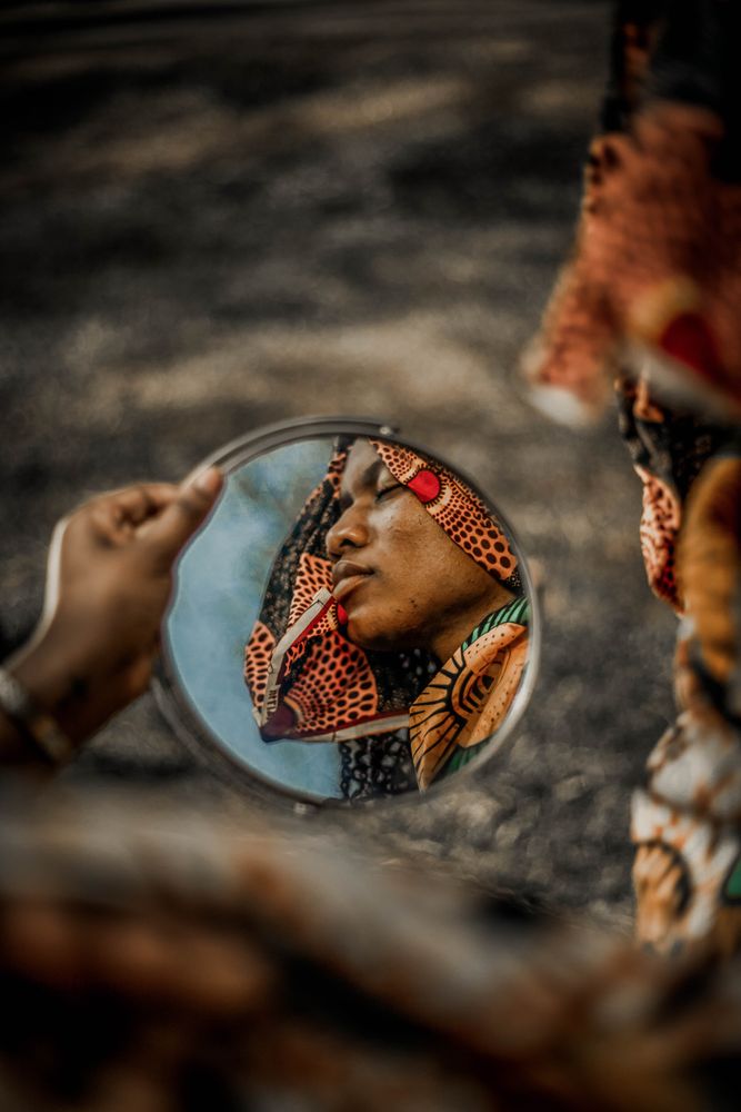 Side view of woman in colorful headscarf reflection on round mirror