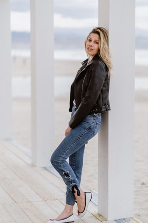 Smiling trendy woman leaning on white pillar on seashore
