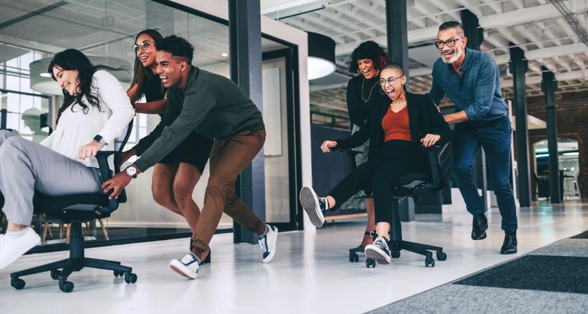 Happy group of colleagues pushing each other on chairs in a modern office
