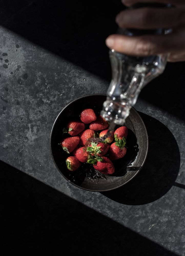Hand with bottle pouring water on strawberries in plate