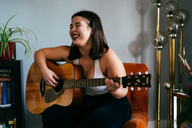 Young multiracial woman laughing while holding her guitar