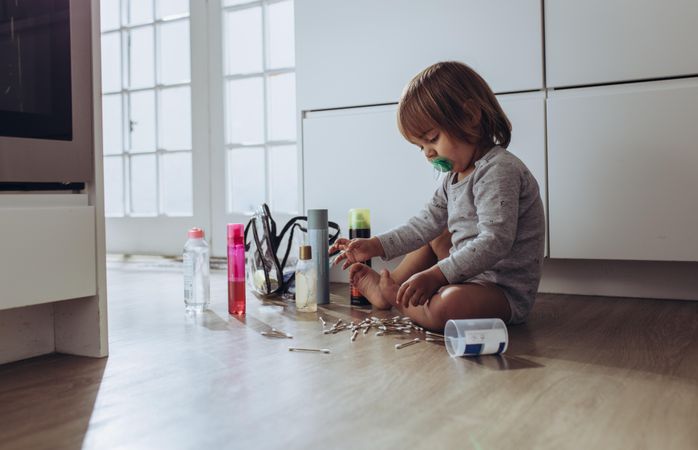 Child sitting on floor at home playing with ear buds and cosmetics