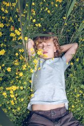 Preteen boy sleeping on green grass and field flowers