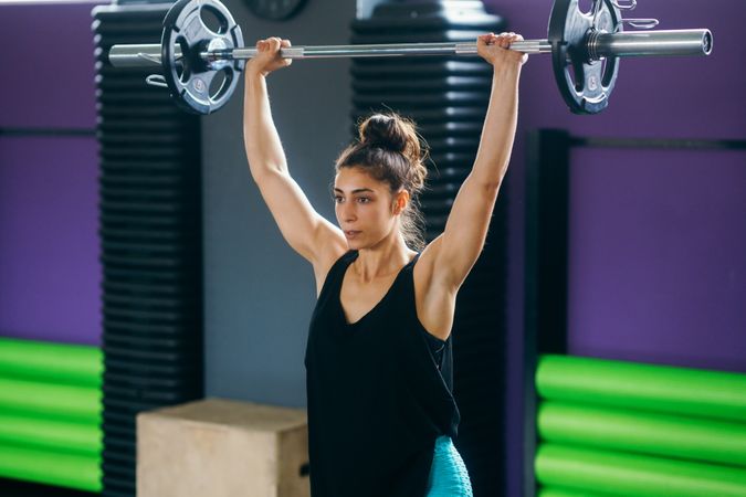 Sporty woman lifting barbell overhead in gym