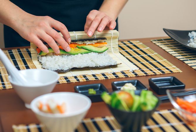 Hands of chef rolling sushi with avocado and salmon