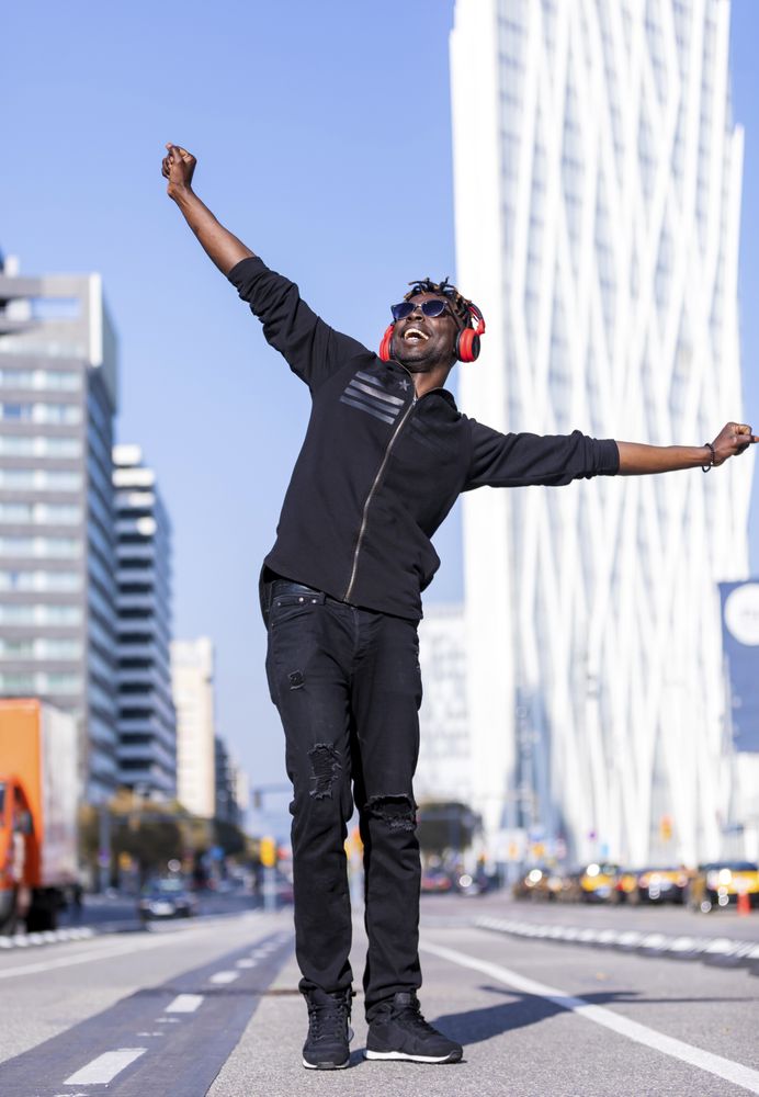 Dancing Black man wearing headphones & sunglasses standing on the street listening to music