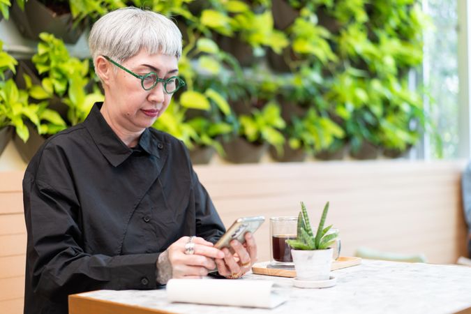 Trendy older woman sitting in cafe looking at phone
