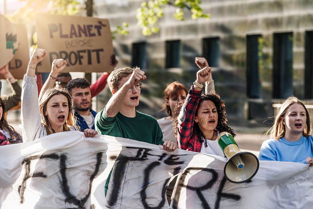 Group of people in their twenties marching with fists raised, megaphones, painted faces, and signs