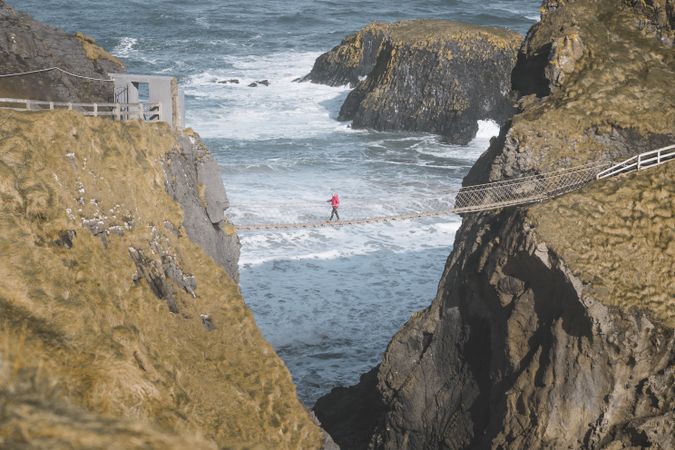 Tourist walking on rope bridge suspended between cliffs in Northern Ireland
