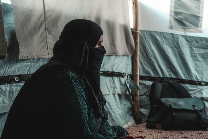Woman in a hijab crying and sitting in a tent