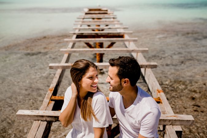 Glad lovers sitting on destroyed pier on seashore