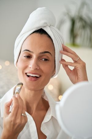 Cheerful woman applying makeup in morning