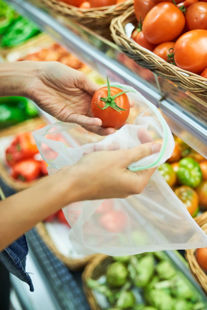 Unrecognizable customer putting tomato into reusable bag