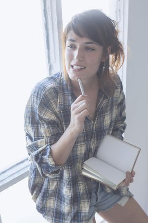 Female in flannel shirt thinking about something with pen to chin with notebook in hand