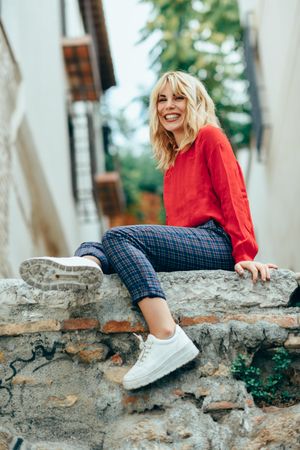 Happy blond woman sitting on stone wall