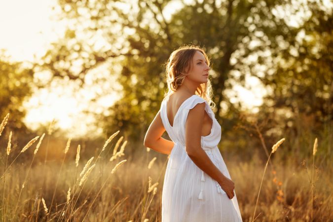 Blonde female in ethereal summer dress turning around in field
