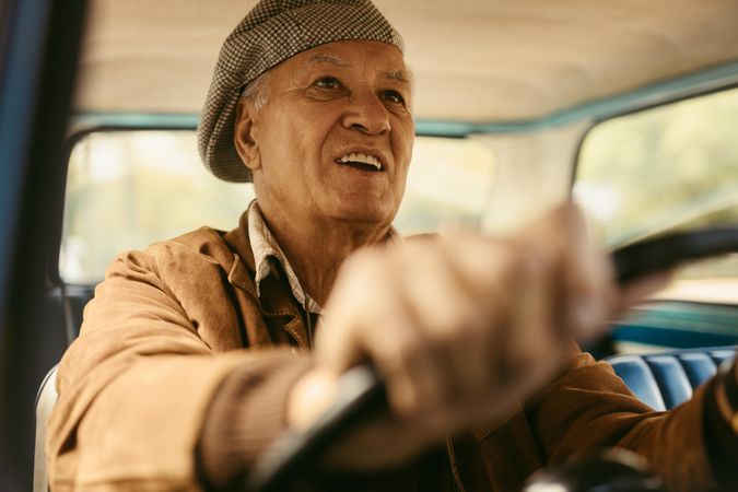 Happy older man wearing a cap enjoying driving a vintage car