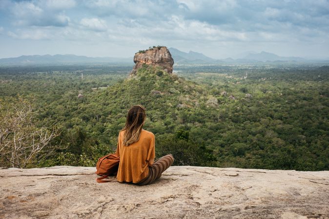 Back of woman sitting on rock taking in view over Sri Lankan forest